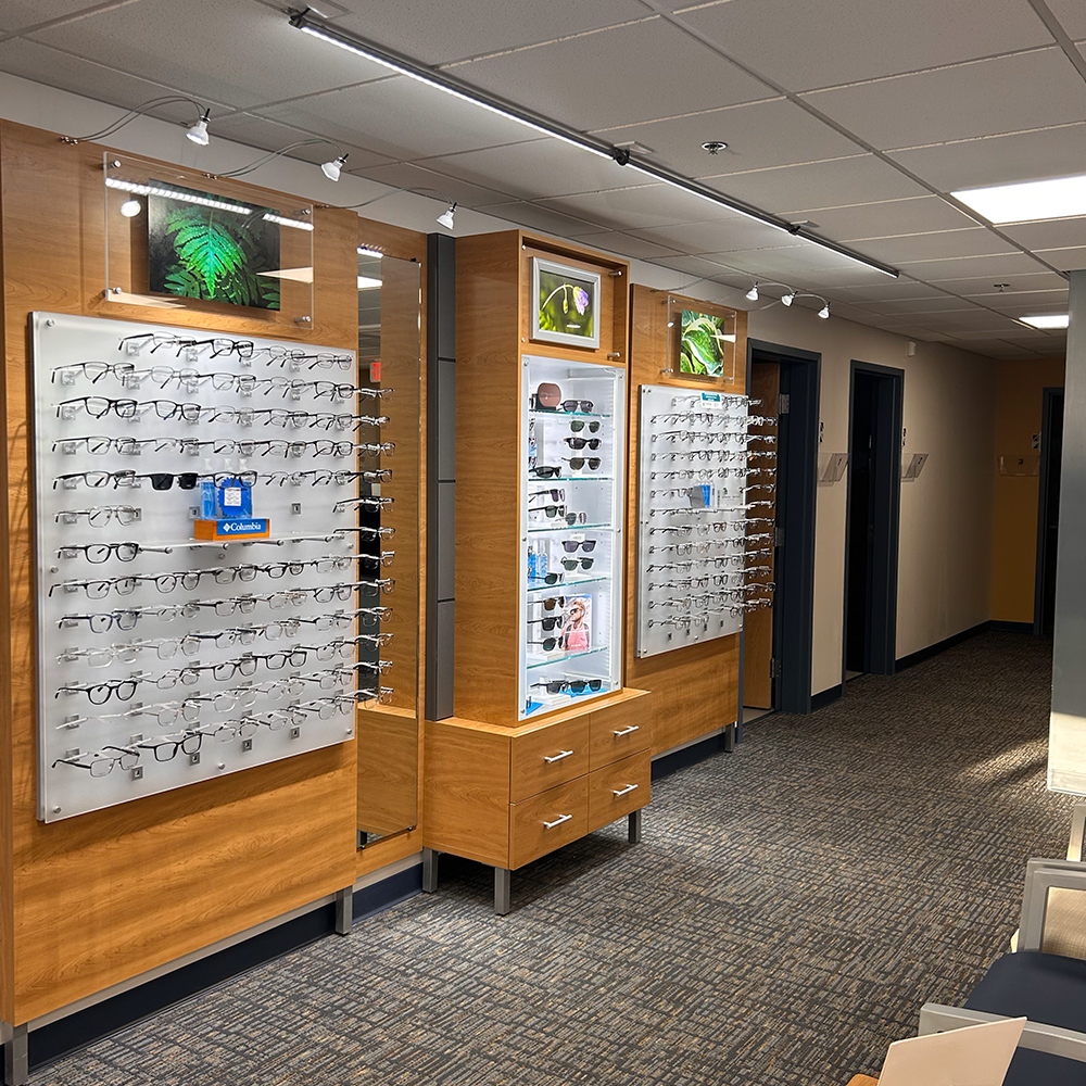 wide angled photo of an eyeglasses and sunglasses display in Amherst Mass at the optical shop of Eye Physicians of Northampton with chairs in the waiting room in the foreground